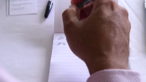 Close-up-of-male-hands-writing-on-a-pad-of-white-paper-with-a-pen