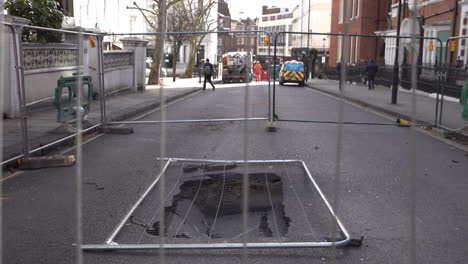 UK-February-2019---People-walk-past-a-fenced-off-sink-hole-that-has-opened-up-in-the-road-in-London’s-affluent-area-of-Kensington