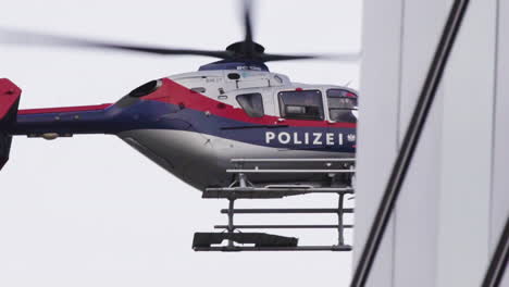 Helicóptero-De-La-Fuerza-Policial-De-Viena-Volando-Detrás-De-Un-Edificio-Con-Ventanas-Reflectantes