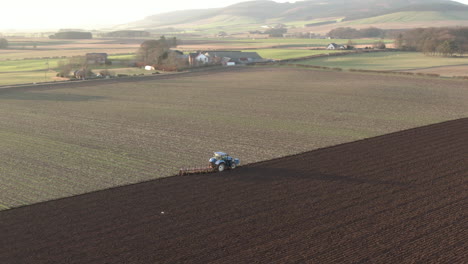 Aerial-view-of-a-farm-tractor-ploughing-a-field-in-Aberdeenshire-on-a-sunny-day,-Scotland