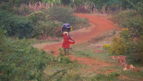 Toma-Amplia-De-Una-Mujer-Africana-Caminando-En-La-Distancia-Llevando-Una-Palangana-De-Ropa-Balanceada-Sobre-Su-Cabeza