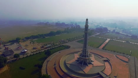 Aerial-view-of-Minar-e-Pakistan-with-its-amusement-park,-Against-the-sun,-A-national-monument-located-in-Lahore,-Pakistan
