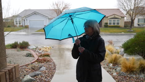 A-beautiful-old-woman-walking-in-the-rain-and-putting-away-her-blue-umbrella-with-raindrops-falling-in-slow-motion-during-a-winter-storm