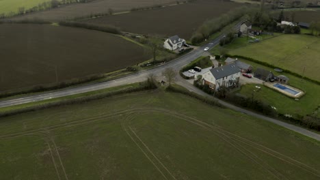 Aerial-view-flying-down-towards-farm-across-green-fields