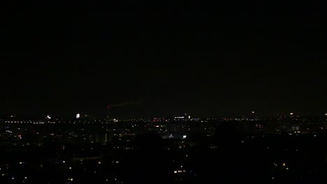 Zwei-Silhouetten-Von-Menschen,-Die-Auf-Einem-Hügel-Stehen-Und-Die-Nächtliche-Skyline-Der-Stadt-Mit-Feuerwerk-überblicken