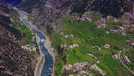 Aerial-flight-over-the-village-houses-with-beautiful-scenes-of-mountains-and-blue-fresh-river,-as-well-as-charmingly-crafted-greenery-with-a-roads