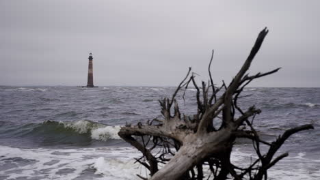 Morris-Island-Lighthouse-Vor-Der-Küste-Von-South-Carolina-Im-Hintergrund-Als-Brandung-Im-Vordergrund-Abstürzt