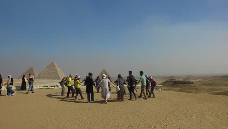Camera-following-tourists-who-are-dancing-in-group-and-holding-hands-for-the-cameras-in-front-of-the-Giza-pyramid-complex