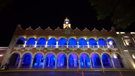 Pushing-in-to-the-Municipal-building-at-dusk-with-its-blue-lights-next-to-the-plaza-grande-in-Merida,-Mexico