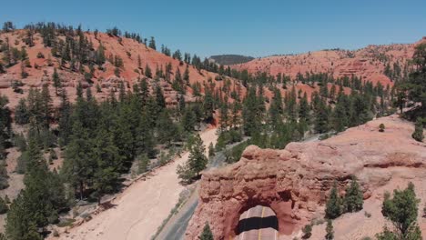 Aerial-footage-over-a-road,-red-rock-and-a-tunnel-with-cars-passing-through