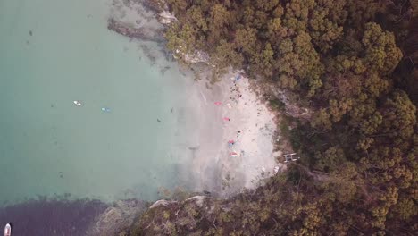 Drone-View-Over-Secret-Beach-With-People-In-Kayak-And-Playing-In-Aqua-Water-And-Trees,-Bruny-Island,-Tasmania,-Australia