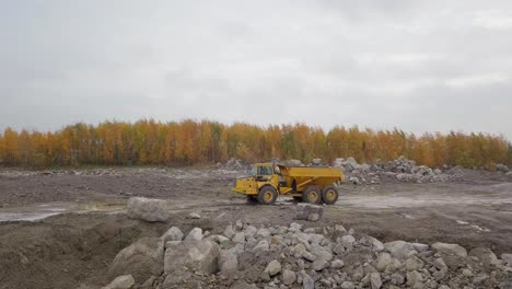 Aerial,-drone-shot,-following-around-a-Articulated-Truck-driving-towards-a-Crawler-Excavator,-Volvo-EC380EL,-digging-at-a-sandpit,-in-Pohjanmaa,-Finland