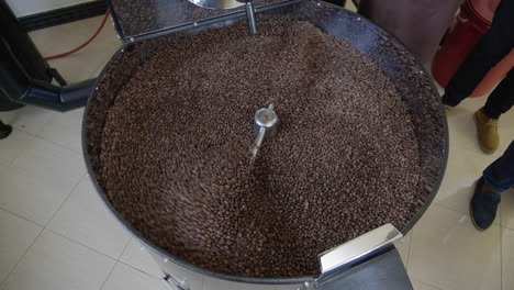 Coffee-roasting-machine-drum-with-roasted-coffee-beans-pouring-into-it-after-roasting