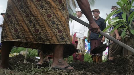 Slow-motion,-low-angle-view-of-Balinese-males-digging-dirt-grave-during-funeral-ceremony