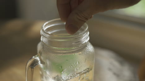 Adding-mint-and-tea-leaves-into-glass-mug-with-boiling-water