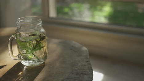 Herbal-tea-in-glass-mug-sitting-on-wooden-table-by-window