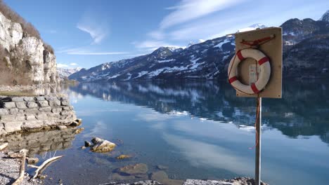 Cinturón-De-Vida-Rojo-Y-Blanco-En-Un-Poste-En-Un-Impresionante-Panorama-Del-Lago-De-Montaña-De-Invierno-En-Suiza