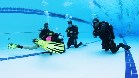 A-female-scuba-instructor-teaching-a-young-child-and-mother-how-to-scuba-dive-in-a-pool
