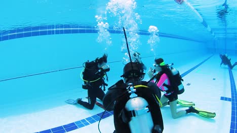 A-female-scuba-instructor-teaching-a-young-child-and-mother-safety-procedures-in-a-swimming-pool