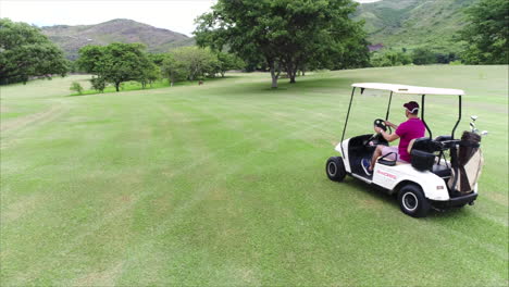 AERIAL-SLOW-MOTION:-Side-shot-of-guy-driving-golf-cart-at-golf-course