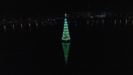 Slow-aerial-backward-panning-from-the-tallest-floating-Christmas-tree-in-the-world-with-changing-lights-in-the-city-lake-of-Rio-de-Janeiro,-Brazil,-2018