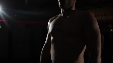 Dark-lit-medium-close-up-on-an-MMA-fighter-standing-in-a-gym