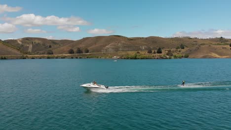 SLOWMO---Waterskiing-behind-boat-on-Lake-Dunstan-near-Clyde-dam,-Central-Otago,-New-Zealand-with-mountains-and-clouds-in-background
