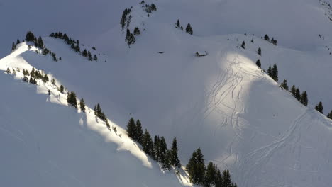 Aerial-view,-flying-up-a-snowy-valley-towards-a-mountain-hut-in-the-French-Alps-in-winter-with-boring-light