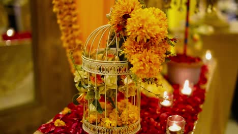 Marry-gold-flower-bouquet-set-in-a-cage-with-Candles-in-glasses-and-rose-petals-on-the-table,-Panning-view