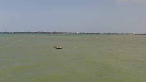 A-man-paddling-the-wooden-fishing-canoe-boat-against-the-waves-on-a-sunny-day-near-the-coast-of-Dar-es-Salaam-city,-Tanzania