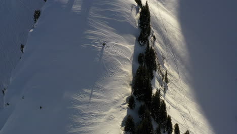 Aerial-view-flying-along-a-snow-covered-mountain-ridge-in-the-French-Alps-in-winter,-with-shadow-and-morning-light