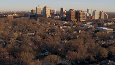 Aerial-pull-away-from-a-city-skyline-and-over-houses-and-trees-at-sunset