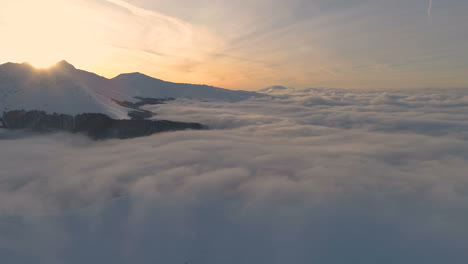 Reverse-drone-shot,-over-a-clouds,-in-front-of-snowy,-mountain-peaks-and-sunset-colors,-in-the-Balkan-mountains,-on-a-sunny,-winter,-dawn,-in-Central-Balkan-National-Park,-Bulgaria