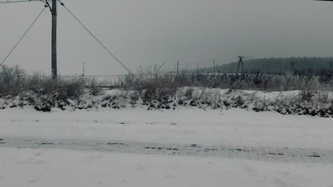 Pov-of-car-travel-passenger-looking-at-roadside-landscape-through-dirty-window-winter-scenery-snow-forest-bare-trees-railway-traction-cloudy-sky