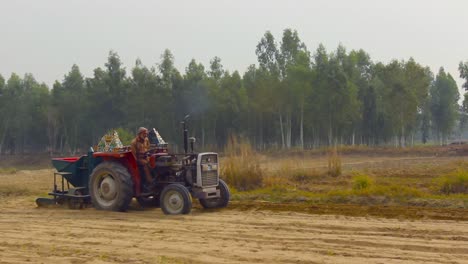 Un-Agricultor-Opera-Su-Tractor-En-El-Campo-Cerca-De-Un-Bosque-De-Eucaliptos,-Vista-Panorámica-Larga