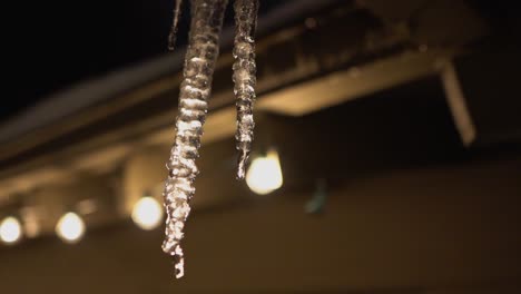 Backlit-Melting-Icicle-hanging-from-roof,-dripping-in-slow-motion