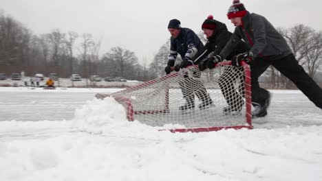Drei-Junge-Männer,-Die-Ihr-Hockeytor-Benutzen,-Um-Schnee-Von-Ihrem-Teich-Hockeyfeld-In-Richtung-Der-Kamera-Zu-Schieben