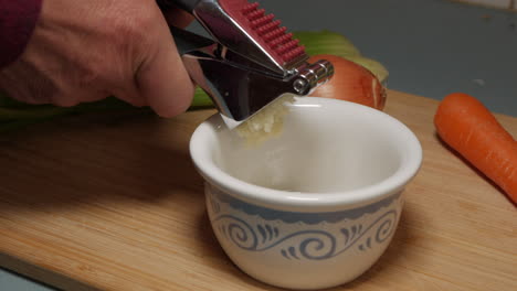 Man-manually-pressing-out-crushed-garlic-with-the-use-of-a-stainless-steel-modern-kitchen-utensil