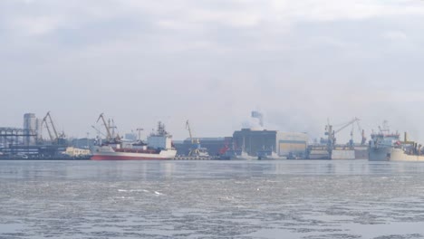 Industrial-port-with-cargo-ships-and-cranes-in-the-distance-with-frozen-ice-cold-water-in-between-on-an-overcast-day