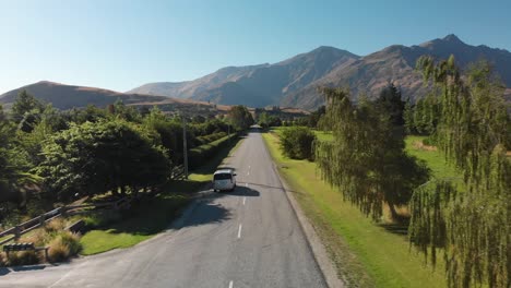 SLOWMO---Luxury-minivan-driving-on-the-road-near-Arrowtown-and-Queenstown,-New-Zealand-with-mountains-in-background