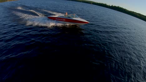 Slow-Motion---Blonde-Caucasian-Female-Drives-Red-and-White-Water-Ski-Boat-on-Blue-Lake-at-Summer-Sunset,-FPV-Drone-Aerial-Track