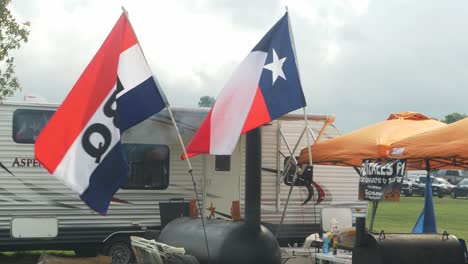 BBQ-Flag-and-Texas-Flag-waving-in-front-of-a-BBQ-Team's-RV-and-Smokers
