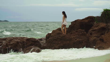 Young-brunette-woman-staying-on-rocks-near-sea-on-stormy-weather