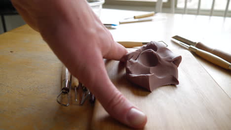 An-artist-carving-and-cutting-brown-modeling-clay-with-a-metal-tool-before-sculpting-and-shaping-the-clay-with-his-fingers-SLIDE-RIGHT