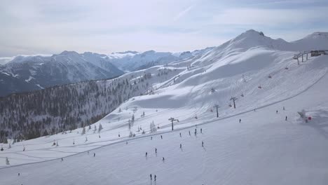 Aerial-swipe-of-a-ski-resort-on-a-sunny-day-with-a-lot-of-people-on-the-ski-slope-and-beautiful-mountains-in-the-background