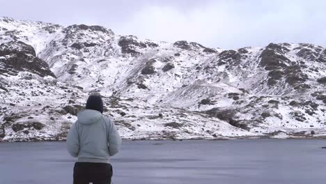 A-man-looking-at-a-frozen-mountain-scene-over-a-tarn-in-winter-in-the-Lake-District