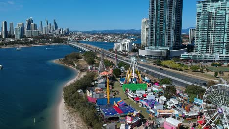 Aerial-view-of-a-colourful-carnival-situated-by-the-sea-with-a-city-skyline-in-the-background