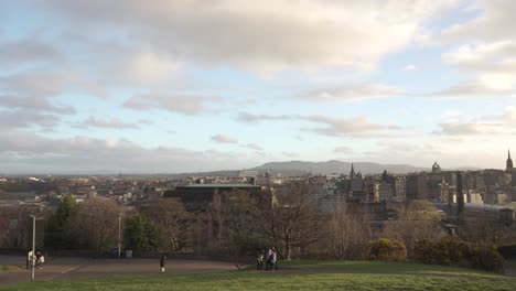 Panning-shot-from-Calton-hill-with-people-walking-and-Nelson-monument-in-the-foreground-with-nice-sunset-light-and-clouds-overlooking-the-city-of-Edinburgh,-Scotland