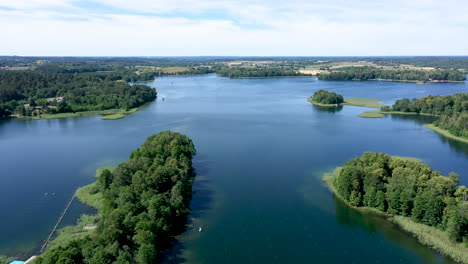 AERIAL:-Reveal-Shot-of-Lake-and-Isolated-Islands-with-Growing-Trees-on-a-Bright-Summer-Day