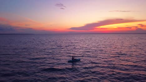 A-dramatic-drone-shot-of-a-lone-kayaker-slowly-driffting-into-a-colorful-sunset